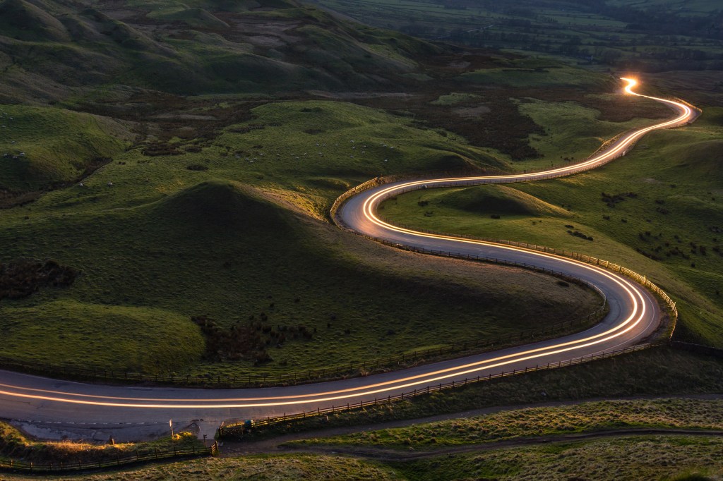 Winding curvy rural road with light trail from headlights leading through British countryside.