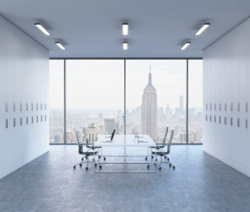 Workplaces in a bright modern open space office. White tables equipped by modern laptops and black chairs. New York panoramic view. 3D rendering.