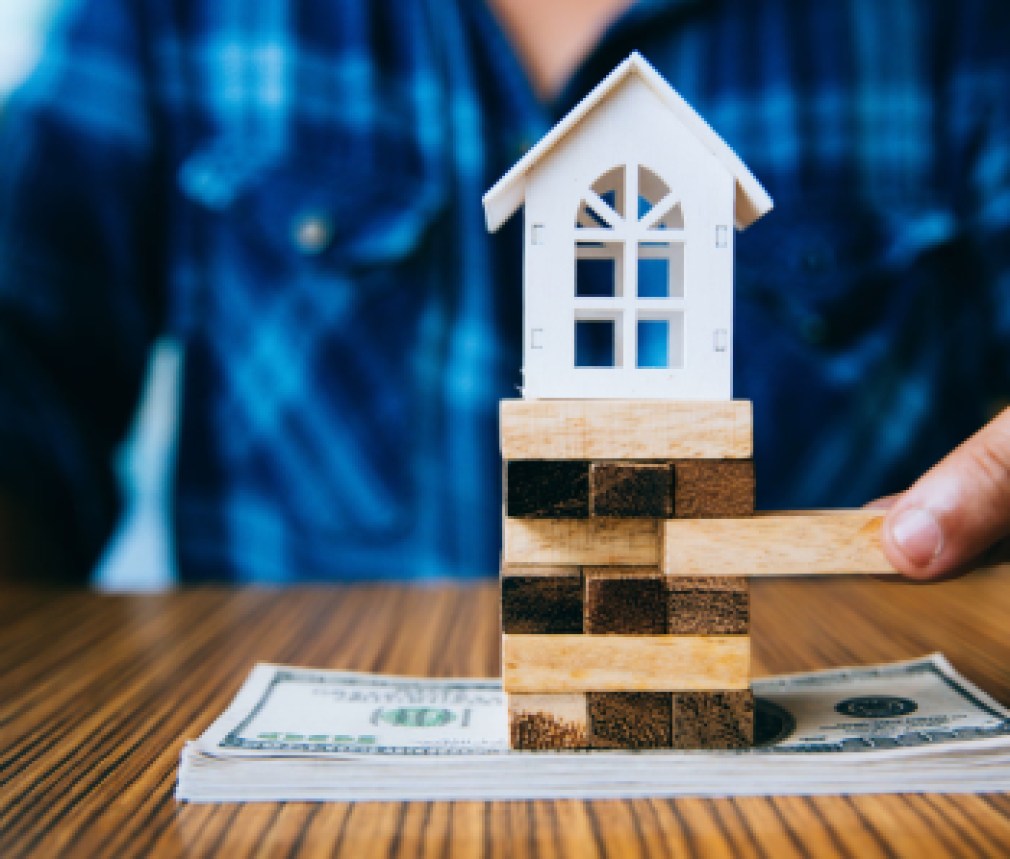 Hand holding a piece of wood block with model white house on dollar banknote. Insurance and property investment real estate concept.