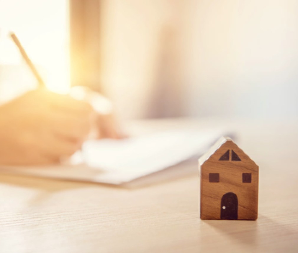 Close up wooden toy house with Woman signs a purchase contract or mortgage for a home, Real estate concept.