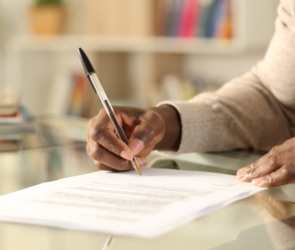 Black man hands signing document on a desk at home