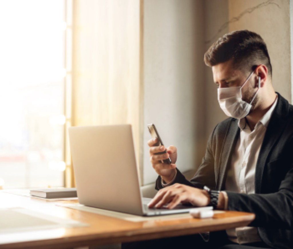 Caucasian adult bearded man indoors in cafe. Lifestyle concept photo with copy space. Picture with handsome guy who using protective face mask. Portrait with gray laptop