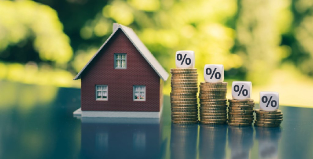 mortgage rates, Symbol for decreasing interest rates. Dice with percentage symbols on decreasing high stacks of coins next to a model house.