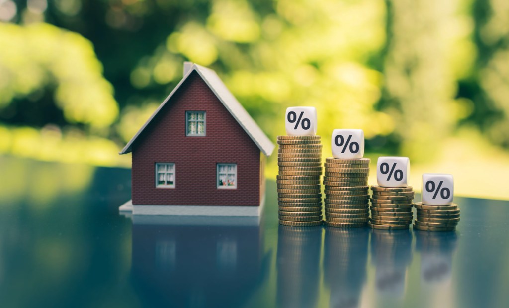 mortgage rates, Symbol for decreasing interest rates. Dice with percentage symbols on decreasing high stacks of coins next to a model house.