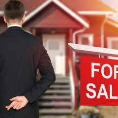 for sale sign in yard of home with real estate agent holding crossed fingers behind back