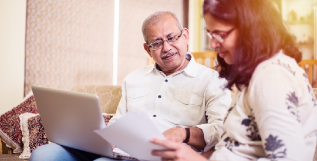 Senior Indian/asian couple accounting, doing home finance and checking bills with laptop, calculator and money while sitting on sofa/couch at home