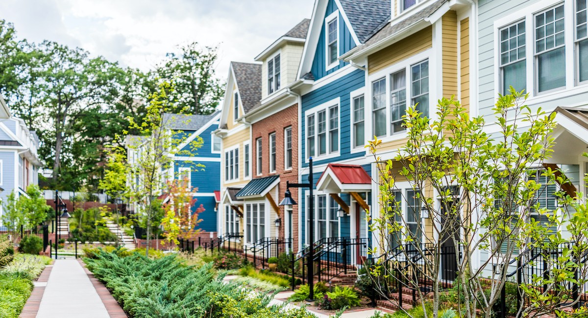 Row of colorful, red, yellow, blue, white, green painted residential townhouses, homes, houses with brick patio gardens in summer