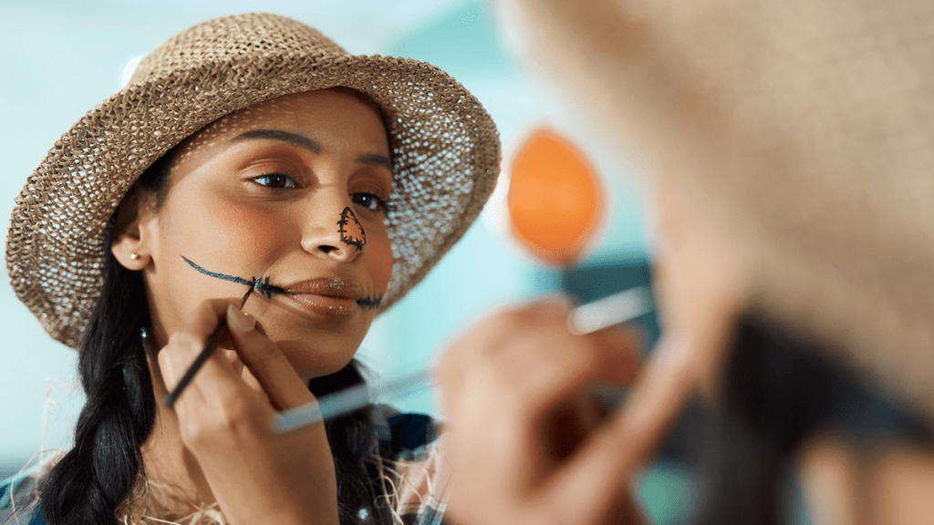 Woman painting her face as the Wizard of Oz' Scarecrow for Halloween